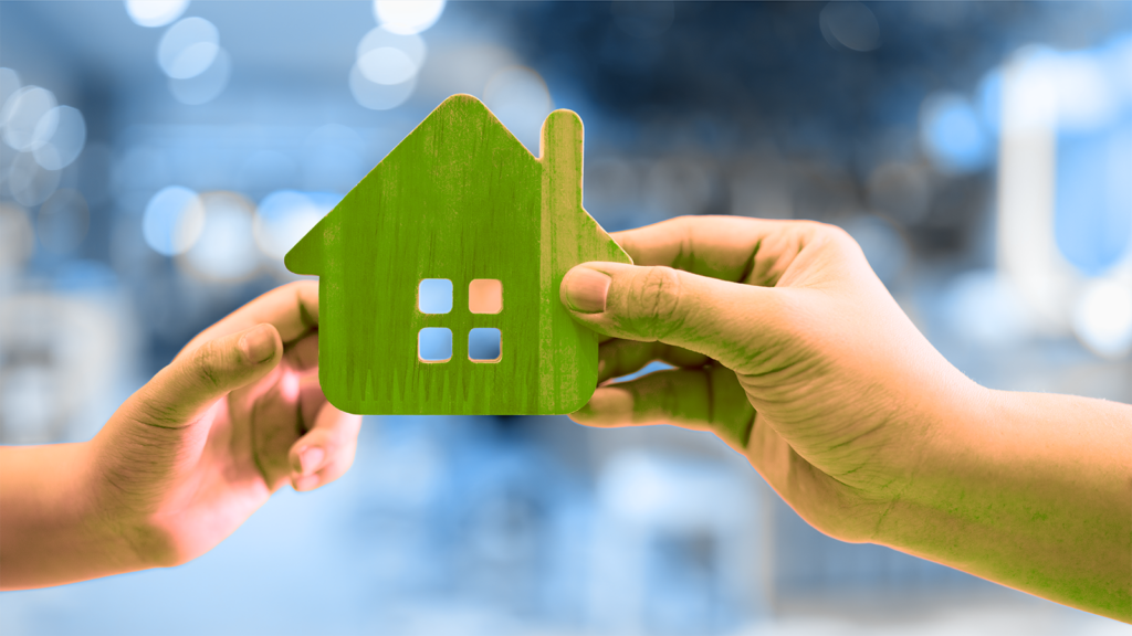 one hand exchanging a cardboard house with another hand, representing a financial gift.